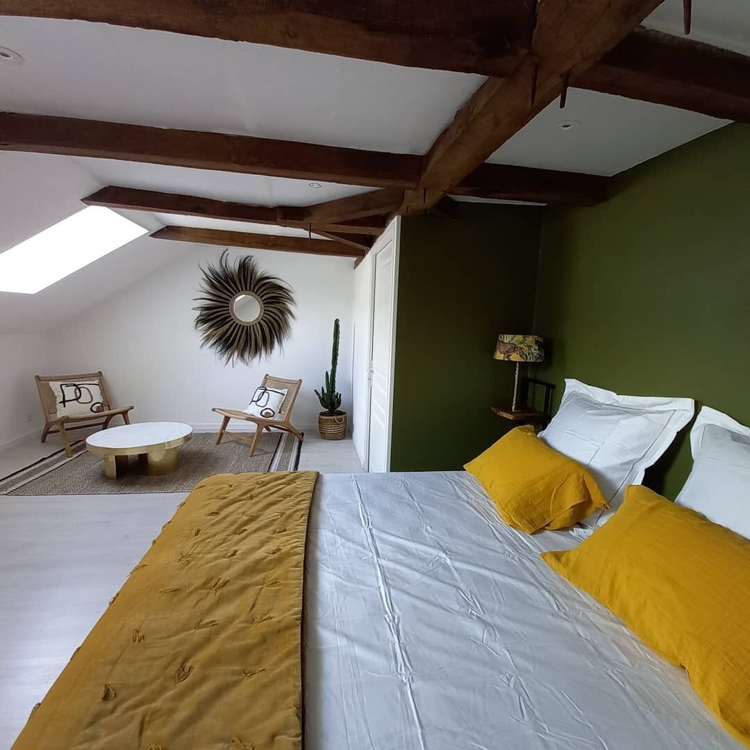 Ein Schlafzimmer mit Bett, Oberlicht, rundem Spiegel, Kaktee und kleinem Tisch mit Stühlen.
