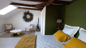 Ein Schlafzimmer mit Bett, Oberlicht, rundem Spiegel, Kaktee und kleinem Tisch mit Stühlen.