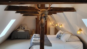Une chambre avec un plafond en pente, une tête de lit en bois, un lit recouvert de draps blancs et une tête de cerf décorative.