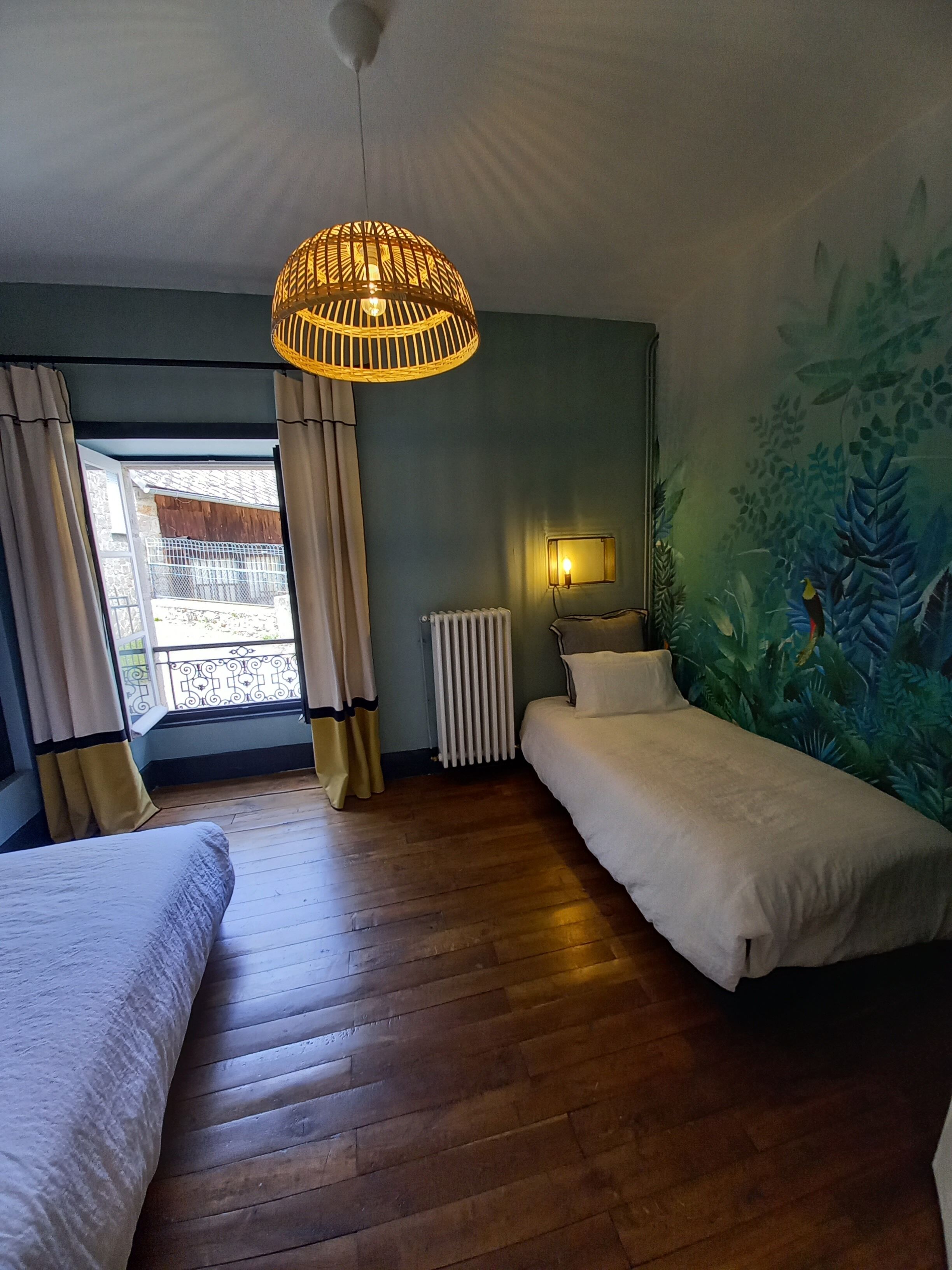 Une chambre avec deux lits, une fenêtre avec des rideaux, un radiateur et une fresque murale.