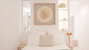 Quarto com cama, uma obra de arte emoldurada, um vaso com flores e uma estante com objetos decorativos.