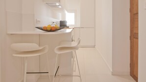 Uma cozinha moderna com armários brancos, bancada e dois bancos altos brancos.