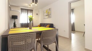 Et moderne spiseområde med et bord dækket til fire personer, to stole, en vase med blomster og en sofa med puder.