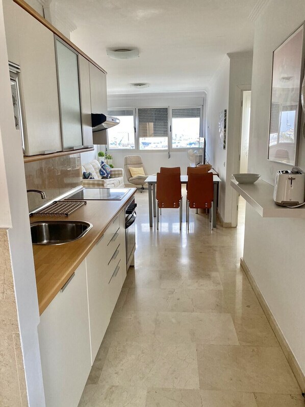 A modern kitchen with white cabinets, a stainless steel sink, and a dining area with two chairs and a table.