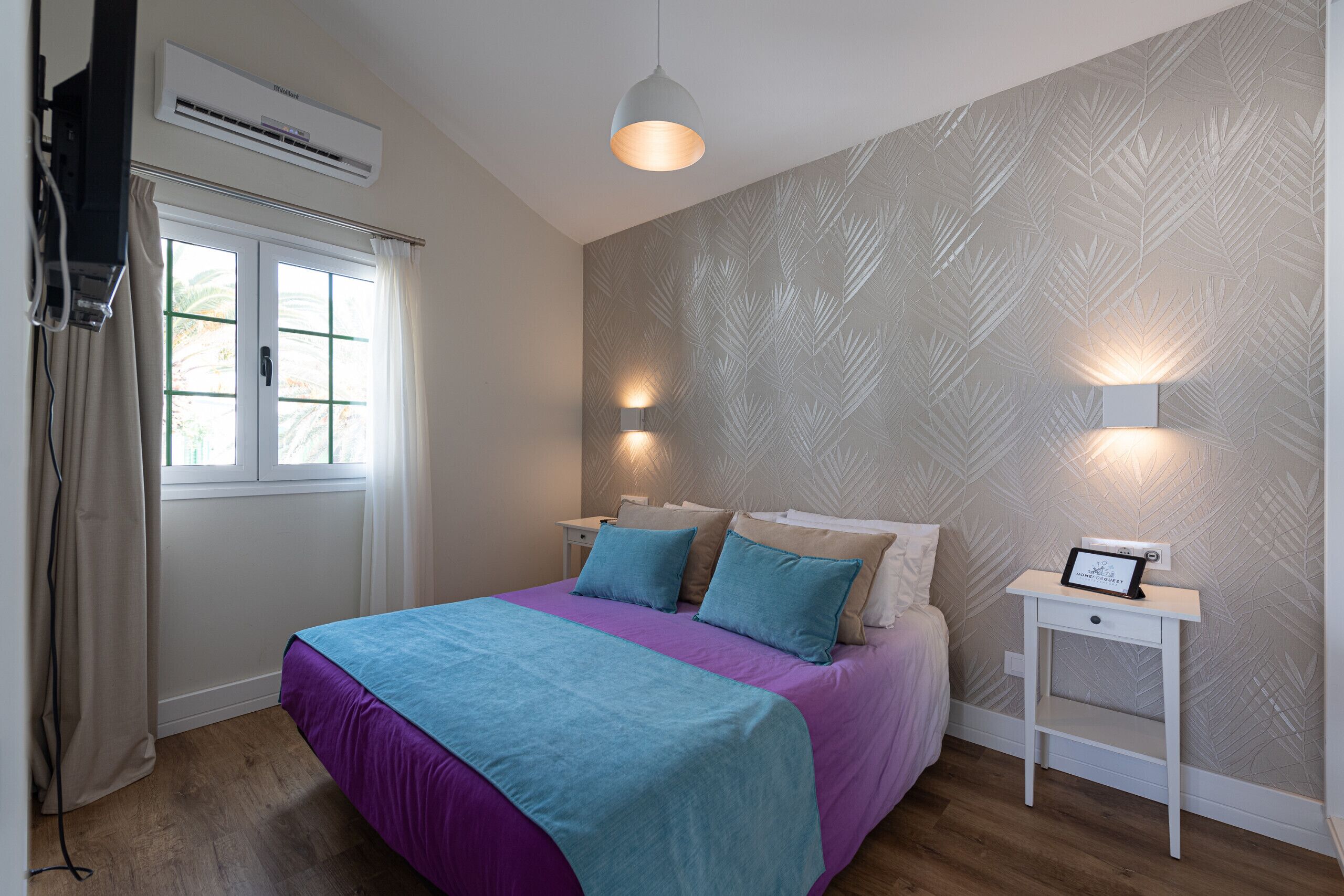 A bedroom with a bed, bedside tables, a wall-mounted air conditioner, and a window with curtains.