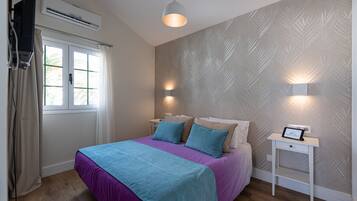 A bedroom with a bed, bedside tables, a wall-mounted air conditioner, and a window with curtains.