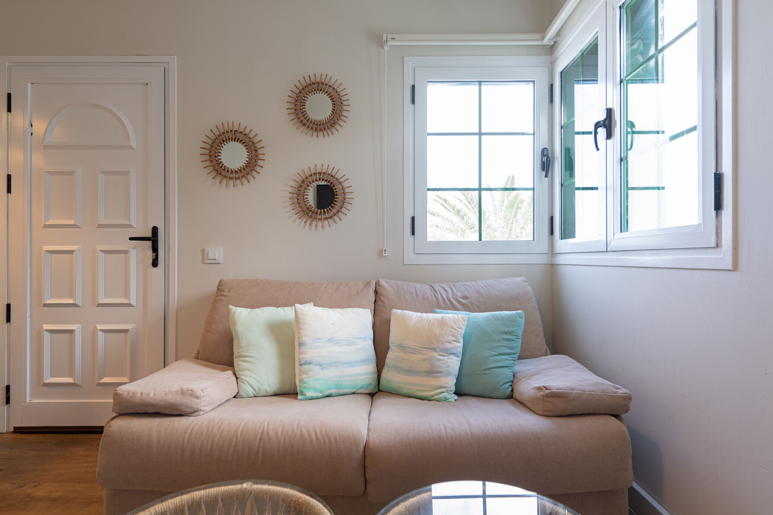 Een woonkamer in neutrale tinten met een beige bank, twee ramen en decoratieve wanddecoratie.