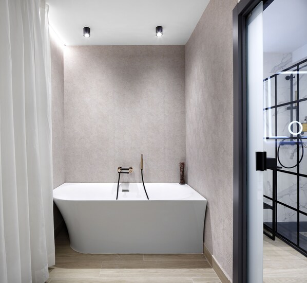 Un baño moderno con una bañera independiente, cabina de ducha con mampara de vidrio y pared con diseño.