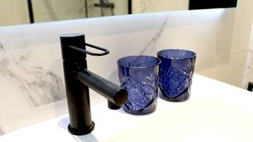 Une salle de bain avec un robinet noir, deux verres bleus et un mur recouvert de carreaux de marbre.