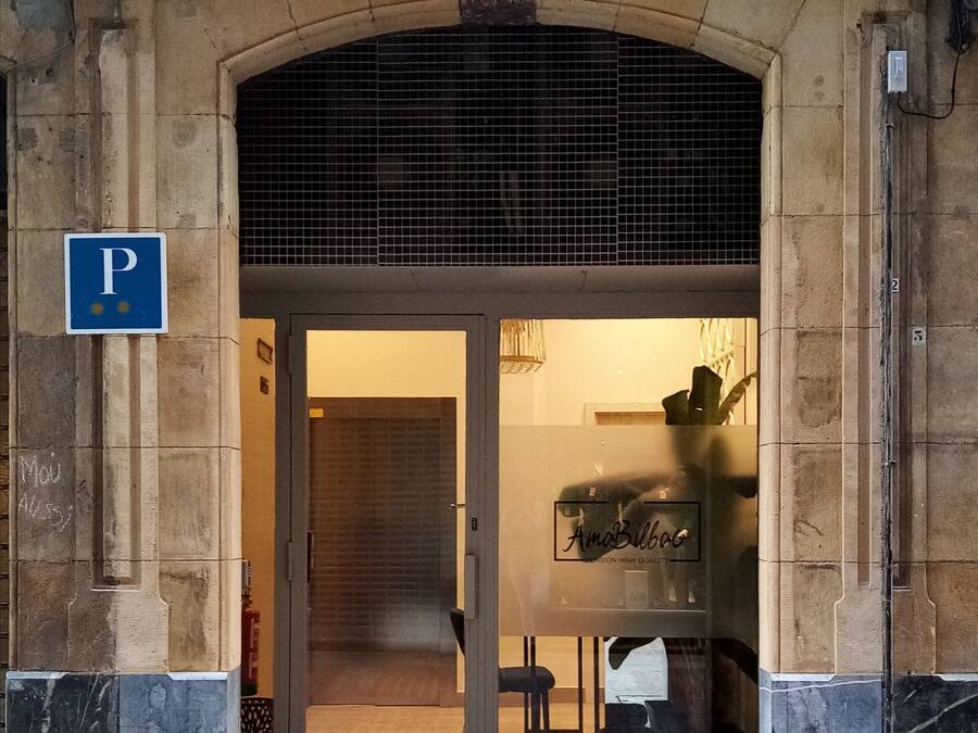 A building entrance with a stone archway, a blue parking sign, and a glass door with a sign reading "AmaBac".