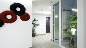 A modern hallway with a potted plant, a glass door, and a wall-mounted light fixture. - Pensión Ama Bilbao (Bilbao)