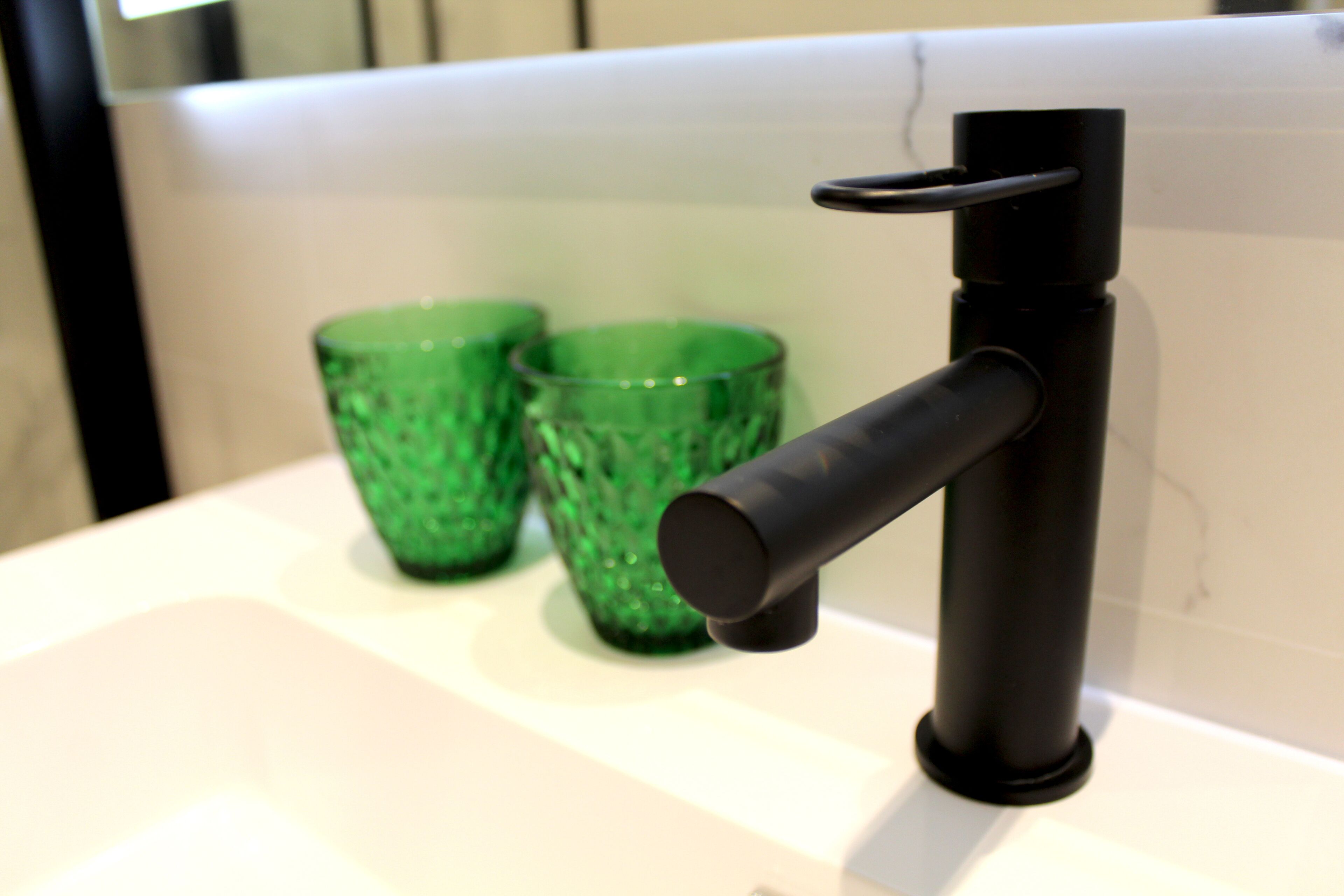 A modern bathroom sink with a black faucet and two green glass cups on the countertop.