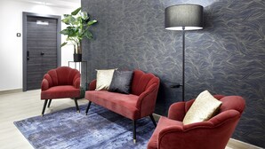A modern room with two red armchairs, a dark patterned wall, a floor lamp, and a potted plant. - Pensión Ama Bilbao (Bilbao)