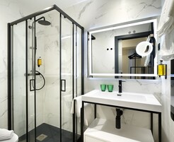 Un bagno moderno con doccia vetro, lavabo bianco con rubinetto nero e uno specchio grande sopra il lavabo.