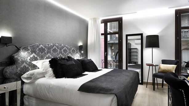 A modern hotel room with a large bed, a desk with a coffee maker, and a view of the city through the window. - Pensión Ama Bilbao (Bilbao)