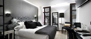 Una habitación de hotel moderna con una cama grande, un escritorio con cafetera y vistas a la ciudad desde la ventana.