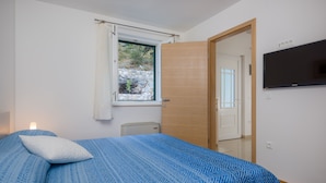 A bedroom with a bed, a window with a view of rocks and greenery, a door, and a wall-mounted TV.