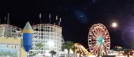 Vista nocturna de un carnaval con noria y montañas rusas.