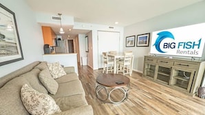 A modern living room with a sofa, a round coffee table, and a dining area with a table and chairs. A kitchen is visible in the background.
