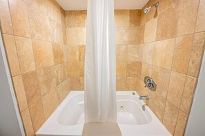 Et badeværelse med badekar, brusehoved og beige flisevægge.
