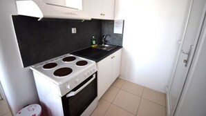 A compact kitchen with a stove, oven, and sink, white cabinets, and a tiled floor.