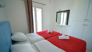 A hotel room with a bed, a blue headboard, a red bedspread, a white pillow, a white blanket, a mirror, and a wardrobe.