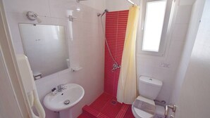 A bathroom with a sink, toilet, shower, and a window.