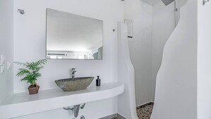 A modern bathroom with a white vanity, a large mirror, a vessel sink, a potted plant, and a shower with a unique curved design. - Fantastic studio for 2 people with private (Mykonos)
