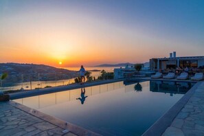 A pool with a sunset view, lounge chairs, and a building with a glass facade.