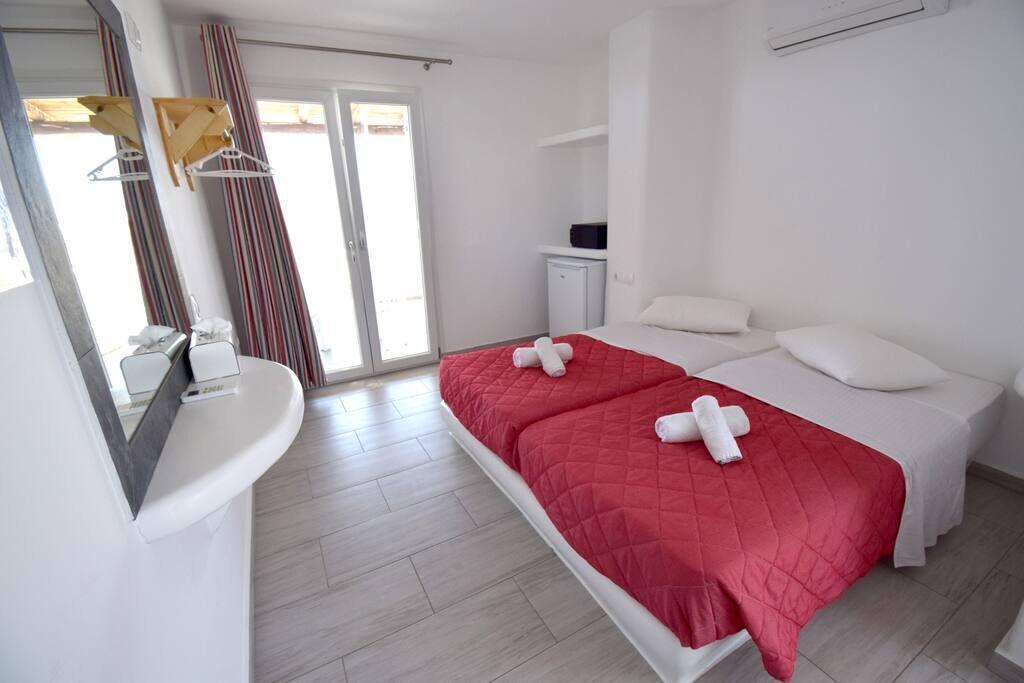 Una camera d'albergo con un letto, un piccolo mobiletto, uno specchio e una finestra con tende.