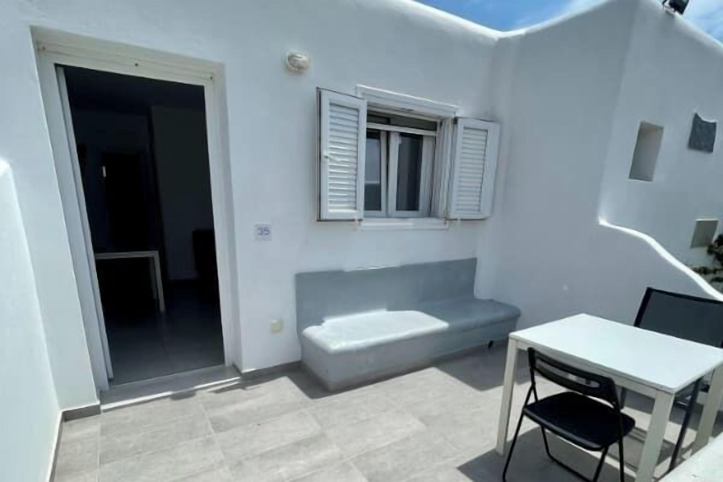 A small, white room with a window, a sofa, and a table.