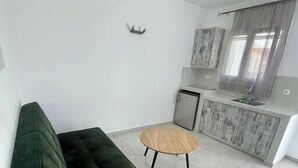 Et moderne opholdsområde med en grøn sofa, et lille træbord og et tekøkken i baggrunden.