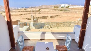 Ein Balkon mit zwei Stühlen und einem Tisch, der auf eine Wüstenlandschaft mit Gebäuden im Hintergrund blickt.