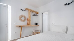 Quarto com cama, prateleira de madeira, espelho, luminária pendente e uma porta.