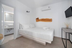 Een moderne slaapkamer met een bed, een houten hoofdbord, een wandtelevisie en een klein tafeltje met een vaas.