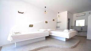 Ein modernes Schlafzimmer mit zwei Betten, einer eingebauten Sitzbank, einem kleinen Badezimmer und einem Fenster.