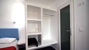 A room with a bed, a white wardrobe with shelves, a glass door, and a small black table. - Large studio apartment for 4 people, in a very (Mikonos)