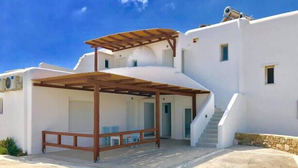 A white building with a covered outdoor seating area, a staircase, and air conditioning units. - Large studio apartment for 4 people, in a very (Mikonos)