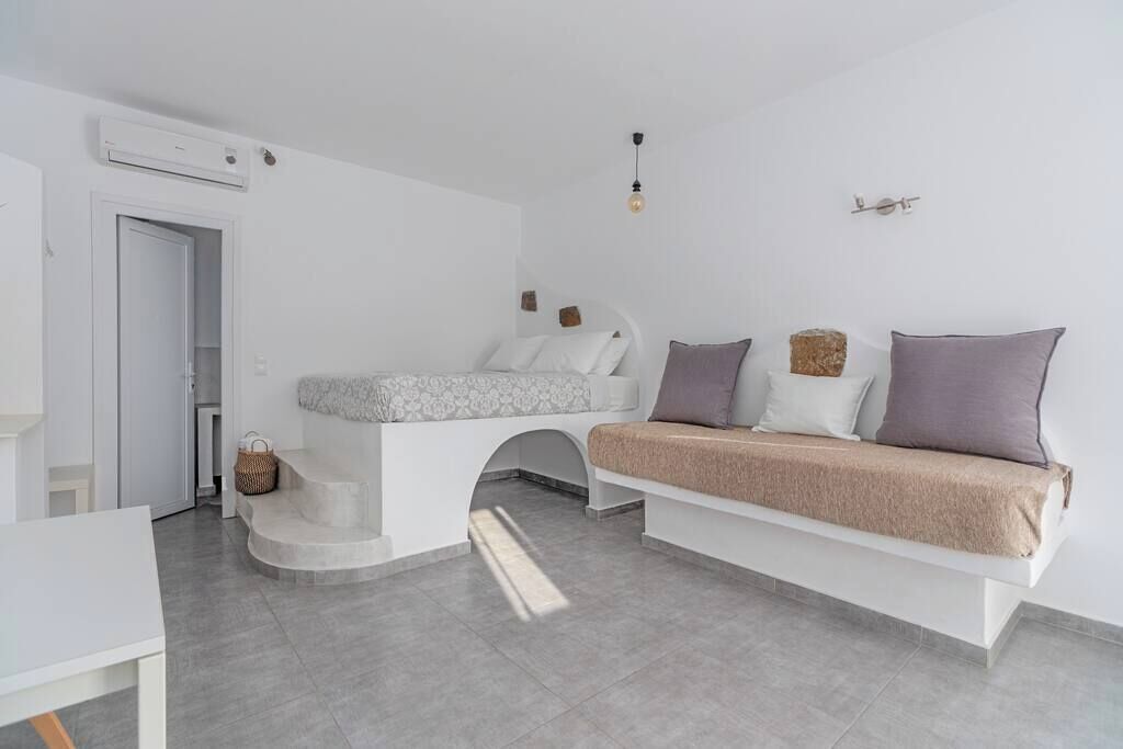 Quarto moderno e minimalista com um banco embutido, uma pequena mesa e uma porta que dá para outro espaço.