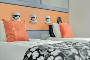 Una habitación de hotel con cama, almohadas y tres cascos de Star Wars sobre el cabecero.