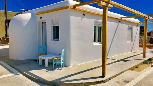 A white building with a small porch, a table, and two chairs. - Apartment for 4 people, located in Vrysi area, (Mikonos)