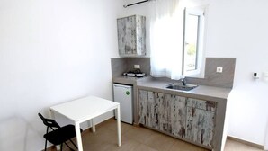 Uma pequena cozinha compacta com mesa e cadeira brancas, pia e geladeira.