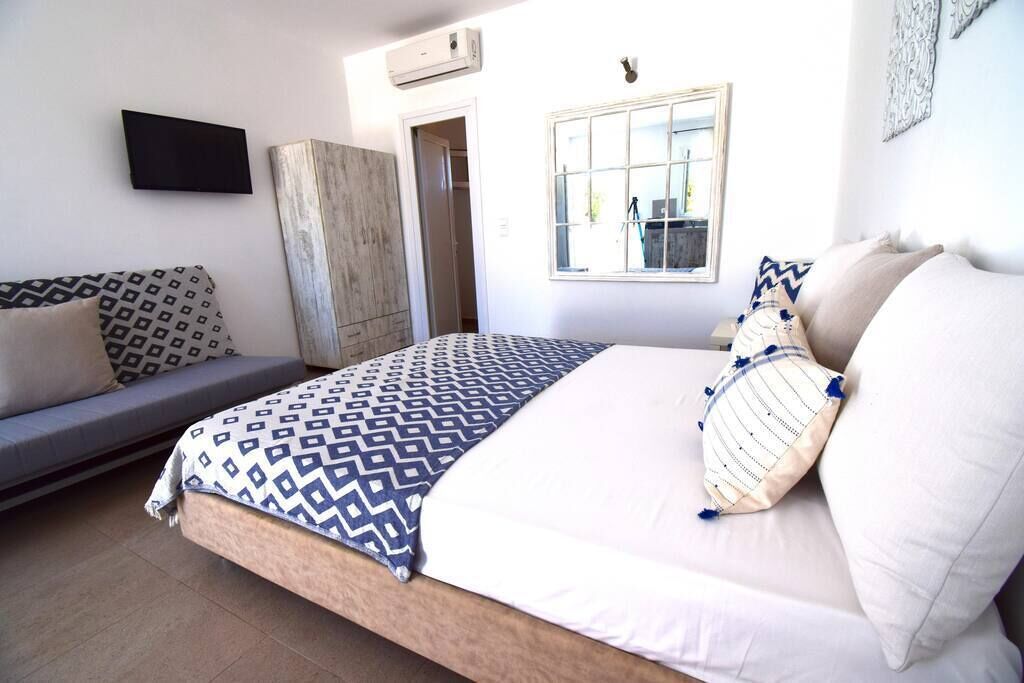A bedroom with a bed, a sofa, a wardrobe, a TV, and a window.