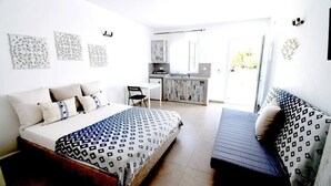 Quarto com cama, sofá, escrivaninha e pequeno espaço de cozinha.