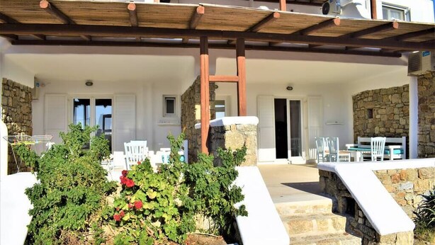 A covered outdoor area with stone walls, white furniture, and a wooden pergola. - Fantastic two-room apartment for 4 people, with (Mikonos)