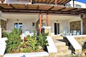A covered outdoor area with stone walls, white furniture, and a wooden pergola. - Private Balcony, Free Parking & Pet-Friendly in (Mikonos)