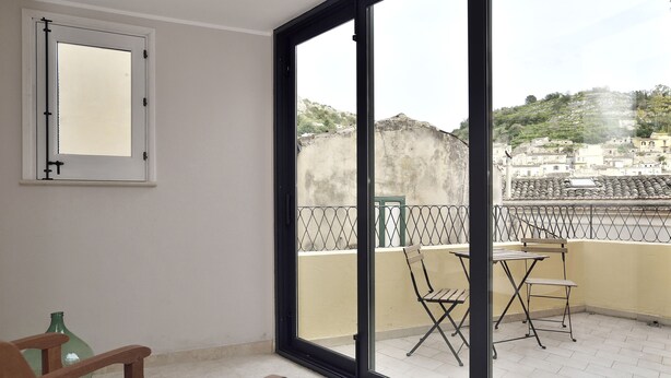 A balcony with a table and chairs, a green bottle, and a window with a mirror. - Old town Modica - newly renovated family home (Modica)
