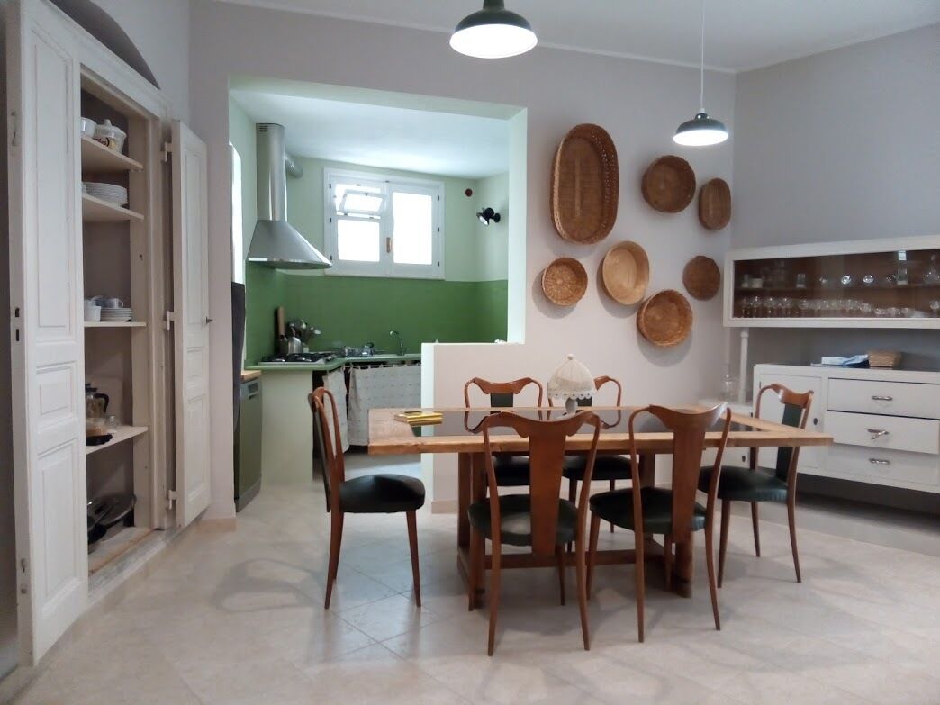 Zona pranzo con tavolo e sedie in legno, una cucina sullo sfondo e piatti decorativi appesi al muro.