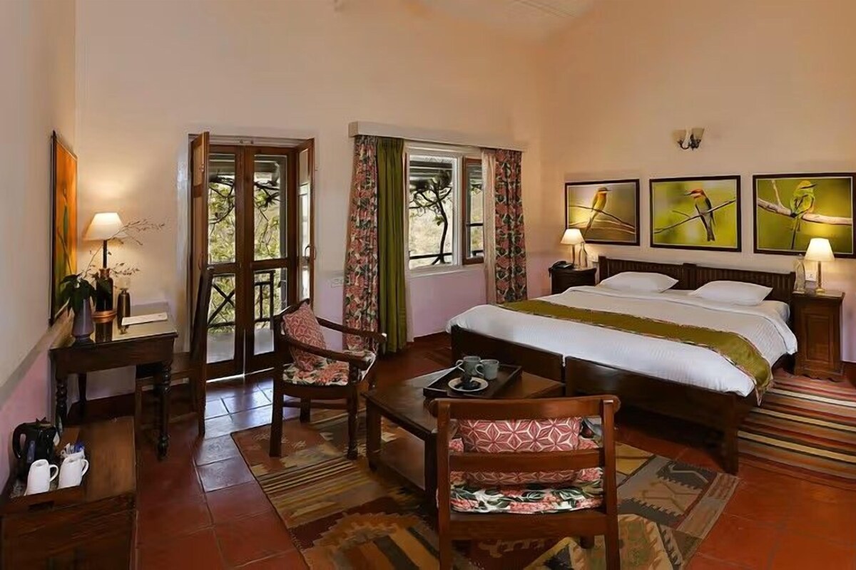 A bedroom with a bed, a chair, a table, a lamp, and a window.