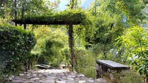 A stone pathway leading through a lush garden with a wooden pergola covered in greenery. - Neemrana’s Glasshouse on the Ganges (Narendranagar)